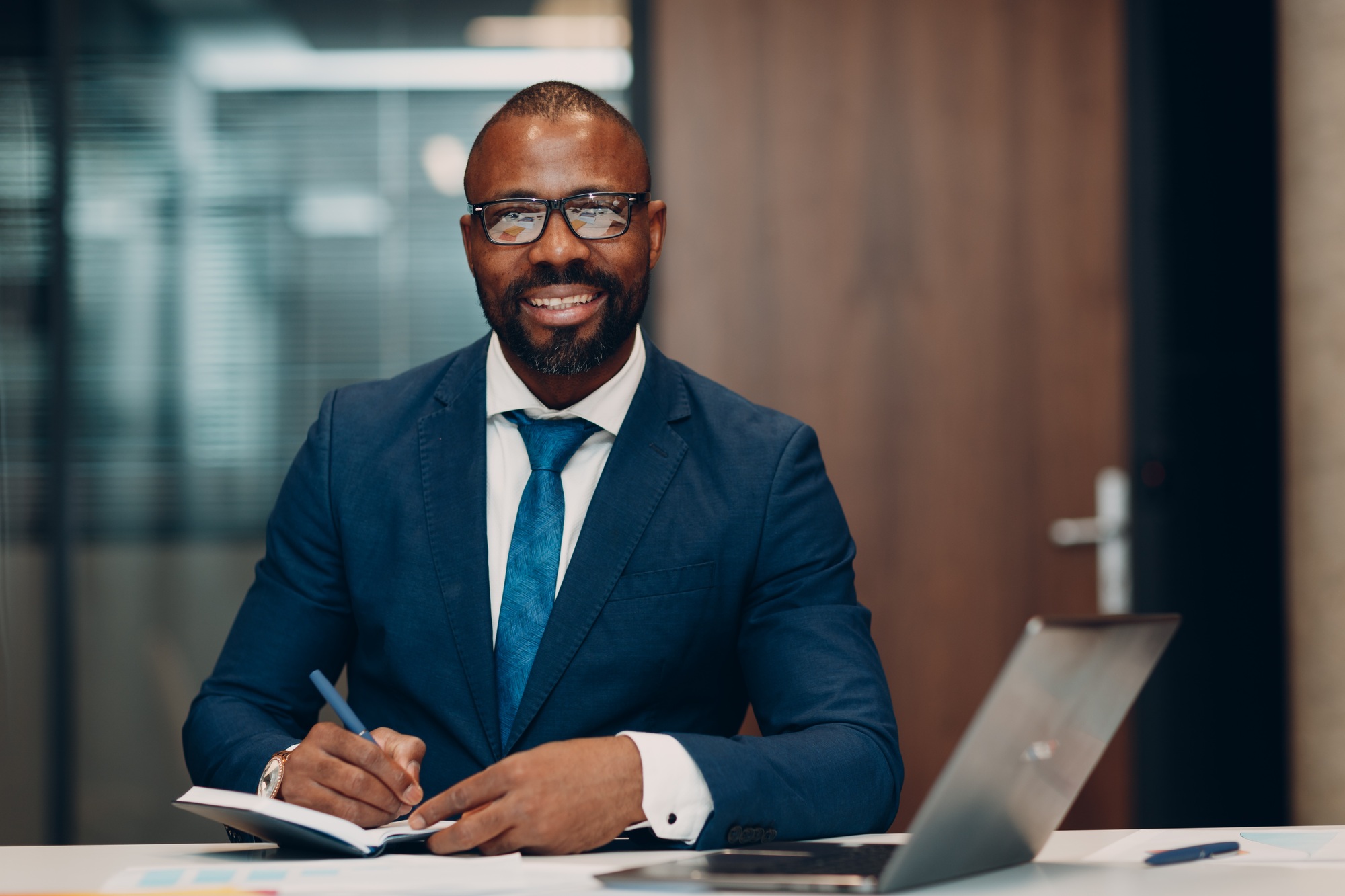Boss smiling african american businessman sitting at table in office with notebook and laptop